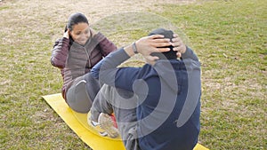 Couple workout outdoors. Latin american young couple do sit ups together on common yellow mat in autumn rainy park as a