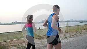 Couple of young adult athletes: woman and man running along promenade of river in modern city. Healthy lifestyle concept