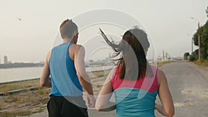 Couple of young adult athletes: woman and man running along promenade of river in modern city. Healthy lifestyle concept