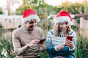 Couple of young adult friends, at Christmas using mobile phone with Christmas hats. video chat and online Christmas shopping
