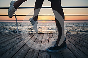 Couple of young hipster lovers kissing, close up on legs and sneakers at the beach at sunrise sky at wooden deck summer time