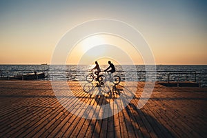Couple of young hipsters cycling together at the beach at sunrise sky at wooden deck summer time photo