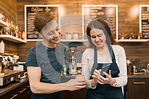 Couple of young male and female coffee shop owners near the counter, talking and smiling, coffee shop business concept photo