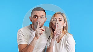 Couple of young man and woman keeps finger on lips, making hush gesture and keep conspiracy