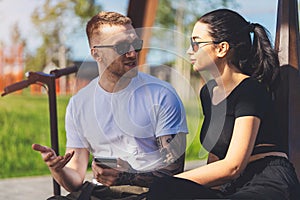 Couple of young man and woman sitting in park on wooden bench