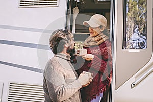 Couple of young mature people enjoy time talking outside the door of a modern camper van during summer holiday travel vacation.