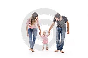 Couple of young parents helping their baby to make first steps on floor in their home