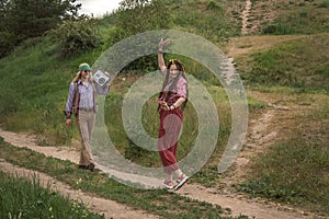 Couple of young people in hippie style on a country road. The girl is dancing, the guy is carrying a retro tape recorder