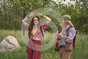 Couple of young people in hippie style. A girl is dancing, a guy is playing a guitar on a country road