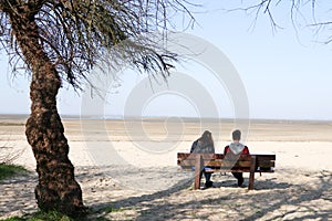 Couple young sitting on a bench in Blue sky and sea beach sand background