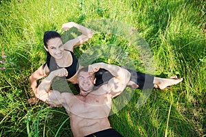 Couple of young sportsmen lie on green grass after workout outdoors