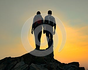 Couple of Young Travelers with Backpack Standing on the Top of the Rock at Summer Sunset. Travel and Adventure Concept