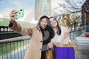 A couple of young women having fun and posing doing a selfie portrait with a cellphone, two girls taking a photo with a