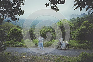 couples of biker pulling small enduro motorcycle on country track among rain falling