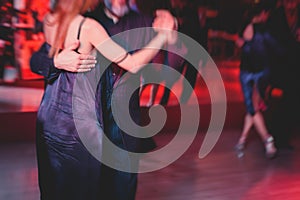 Couples dancing argentinian dance milonga in the ballroom, tango lesson in the red lights, dance festival