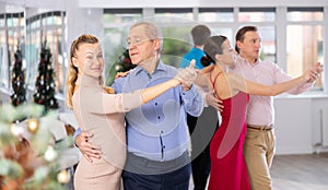 Couples dancing during Christmas - men and women dancing tango or samba next to Christmas tree