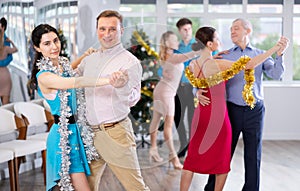 Couples dancing during Christmas - men and women dancing tango or samba next to Christmas tree
