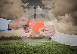 Couples hand holding heart against digitally generated eiffel tower at distance