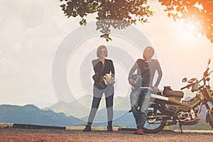 couples holding safety helmet sitting on small enduro motorcycle against beautiful natural mountain scene at khaoyai national