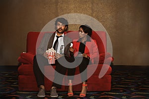Couples sit together in the cinema with movie tickets and popcorn.