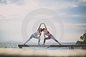 Couples of woman playing yoga pose on beach pier with moring sun light photo