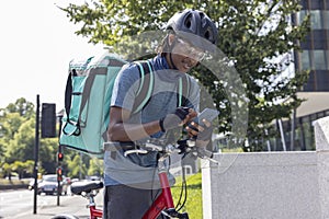 Courier On Bike Delivering Takeaway Food In City Checking Directions And Order Details On Mobile Phone