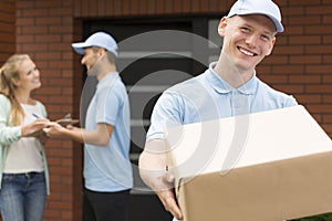 Courier in blue uniform holding big brown package and smiling