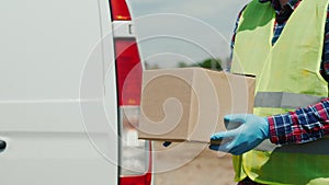 A courier with a cardboard box stands against the background of a white delivery service van