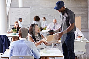 Courier Collecting Package From Businesswoman In Busy Office