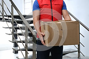 Courier with damaged cardboard box indoors. Poor quality delivery service