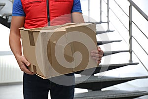 Courier with damaged cardboard box indoors. Poor quality delivery service