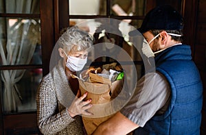 Courier delivering shopping to senior woman with face mask, corona virus and quarantine concept.