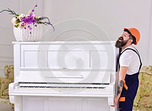 Courier delivers furniture, move out, relocation. Man with beard worker in helmet and overalls lifts up, efforts to move