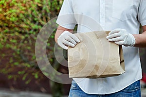 Courier, delivery man in protective mask and medical gloves delivers takeaway food and coffee. Delivery service under quarantine