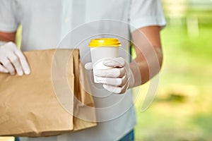 Courier, delivery man in protective mask and medical gloves delivers takeaway food. Delivery service under quarantine, disease out