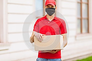 A courier employee in uniform and a protective face mask holds an empty cardboard box outdoors