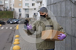 Courier in face mask with a parcel at the entrance of home verifies the information in the documents