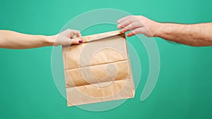 Courier in gloves passing craft shopping bag with delivery against mint background