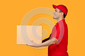 courier guy giving parcel carton box looking aside, yellow backdrop