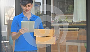 The courier holding a package box is using a tablet to verify the customer`s address