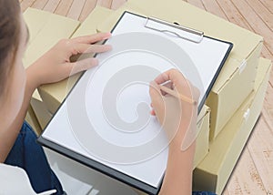 Courier making notes in delivery receipt among parcels on boxes