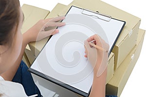 Courier making notes in delivery receipt among parcels on boxes