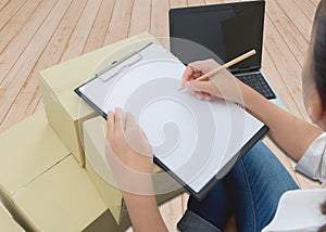 Courier making notes in delivery receipt among parcels on boxes
