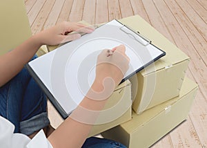 Courier making notes in delivery receipt among parcels on boxes