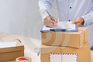 Courier making notes in delivery receipt among parcels at table