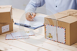 Courier making notes in delivery receipt among parcels at table