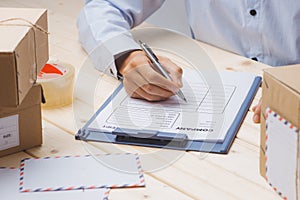 Courier making notes in delivery receipt among parcels at table