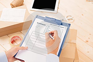 Courier making notes in delivery receipt among parcels at table