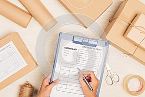 Courier making notes in delivery receipt among parcels at table