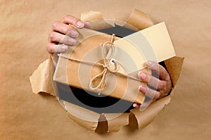 Courier man or postman delivering or giving parcel through torn brown paper background